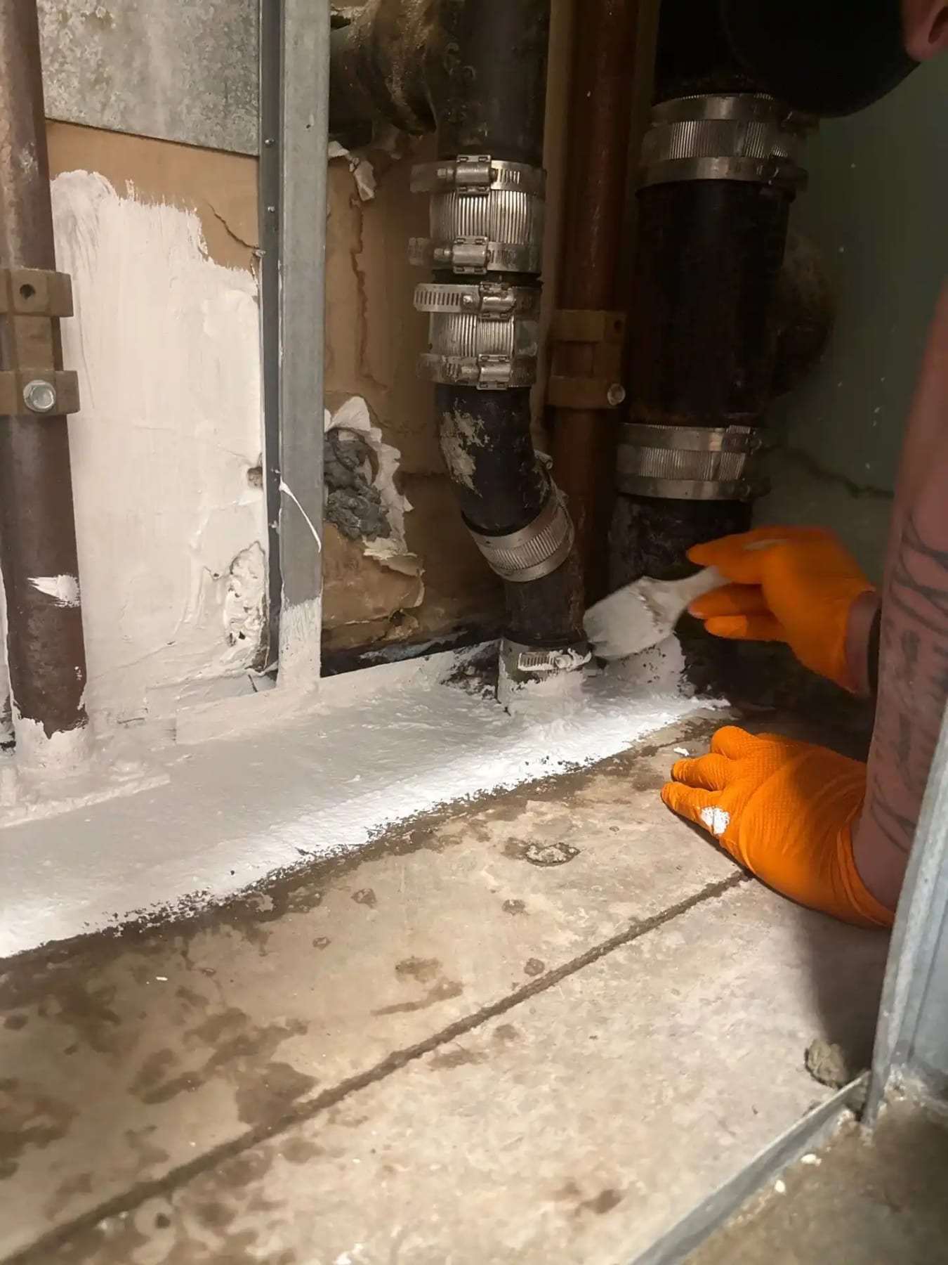 Gloved hand beside corroded supply fittings inside an opened wall