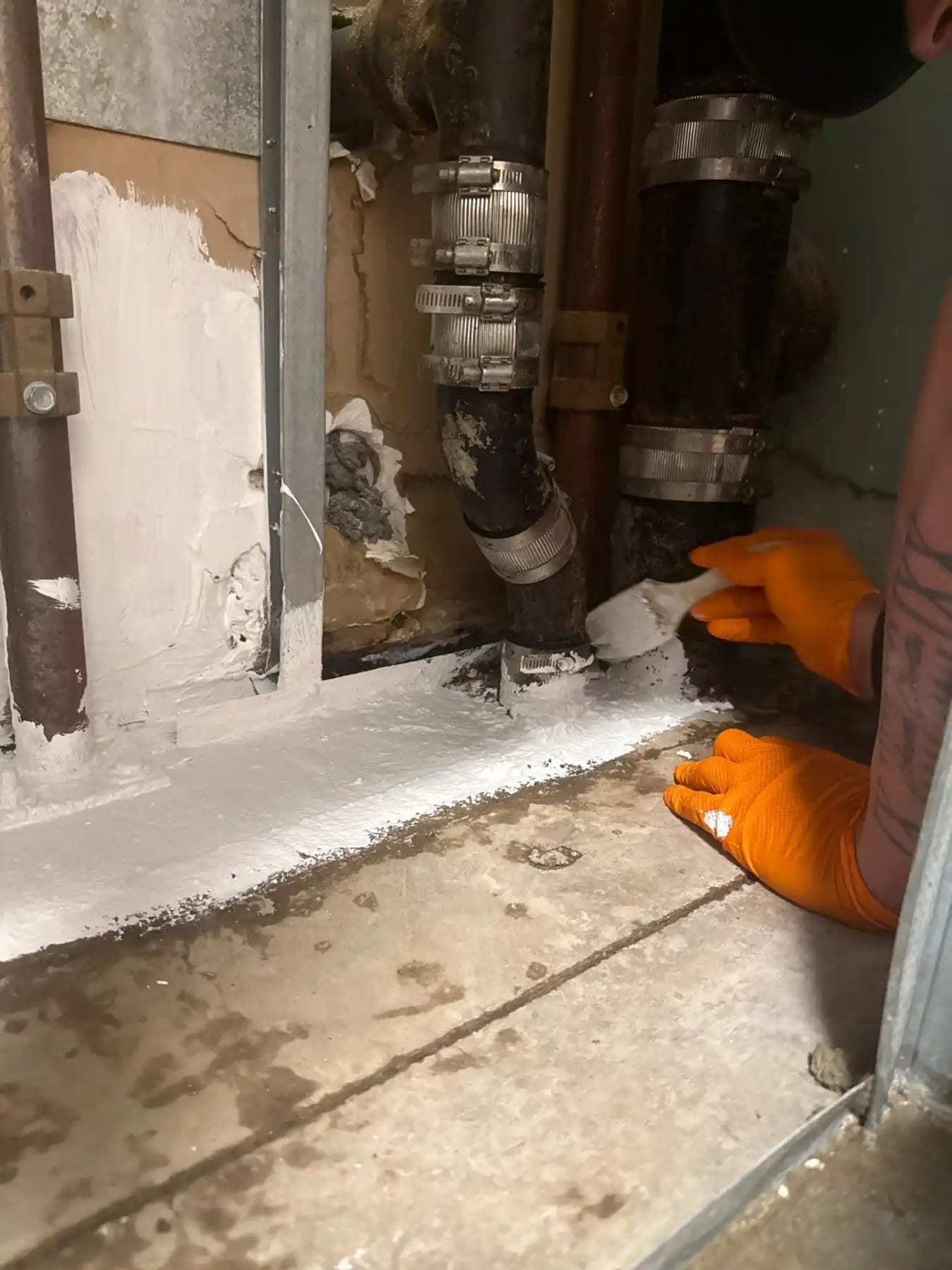 Gloved hand beside corroded supply fittings inside an opened wall