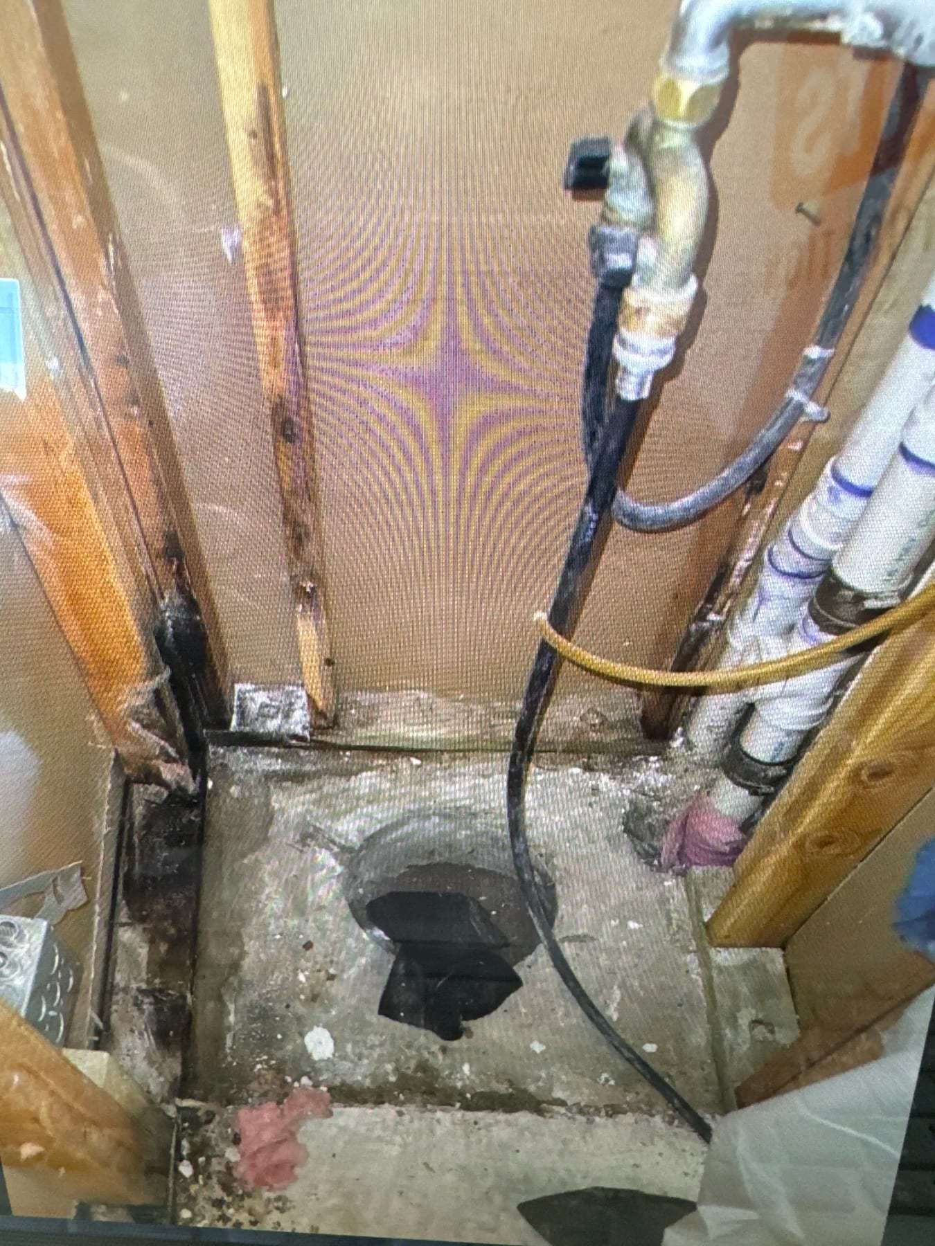Supply and drain plumbing inside an opened wall above a cut subfloor